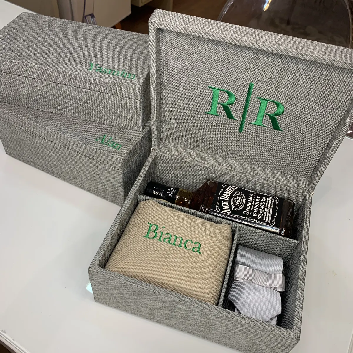 Caixa de padrinho em linho cinza com iniciais bordadas em verde, garrafa de whisky e toalha bordada com nome